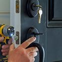 A person is holding a drill and pointing to the door handle.