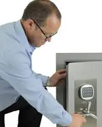 A man in glasses and a blue shirt is putting something into a safe
