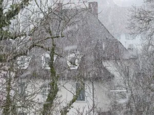 A house with snow falling on it's roof.